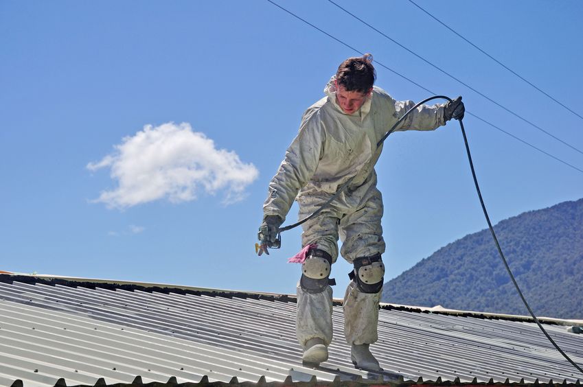 a trademan uses an airless spray to paint the roof of a building