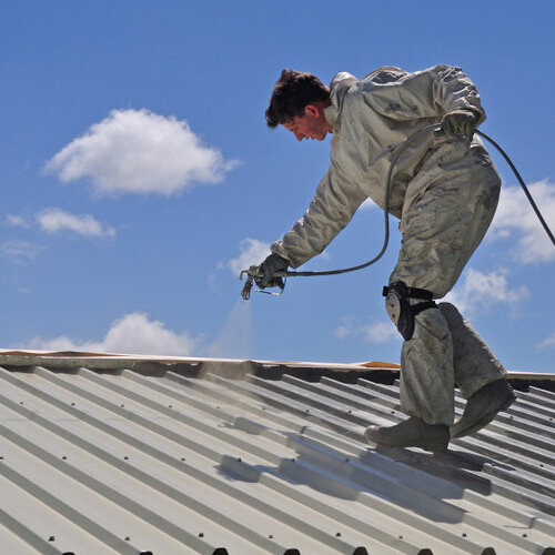 A trademan uses an airless spray to paint the roof of a building